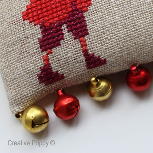 A row of small jingle bells stitched at the base of the cross stitch ornament